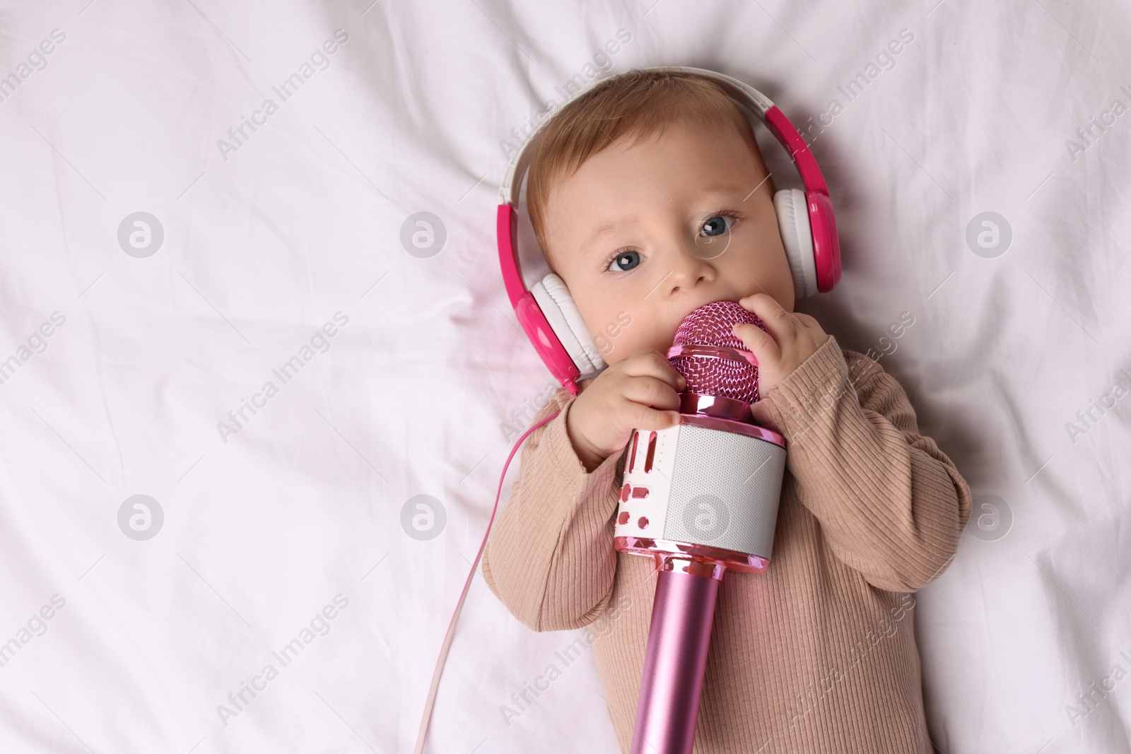 Photo of Cute little baby with headphones and microphone lying on bed, top view