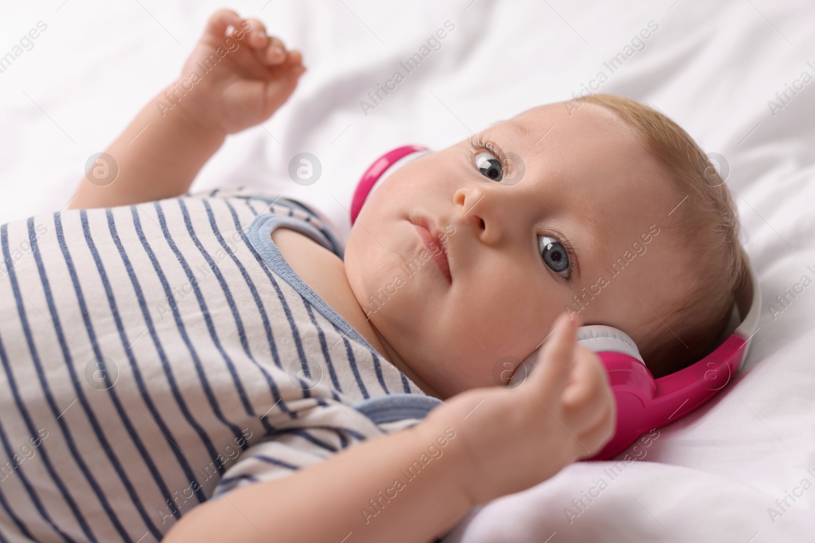 Photo of Cute little baby with headphones lying on bed