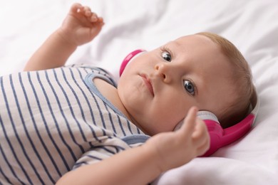 Cute little baby with headphones lying on bed