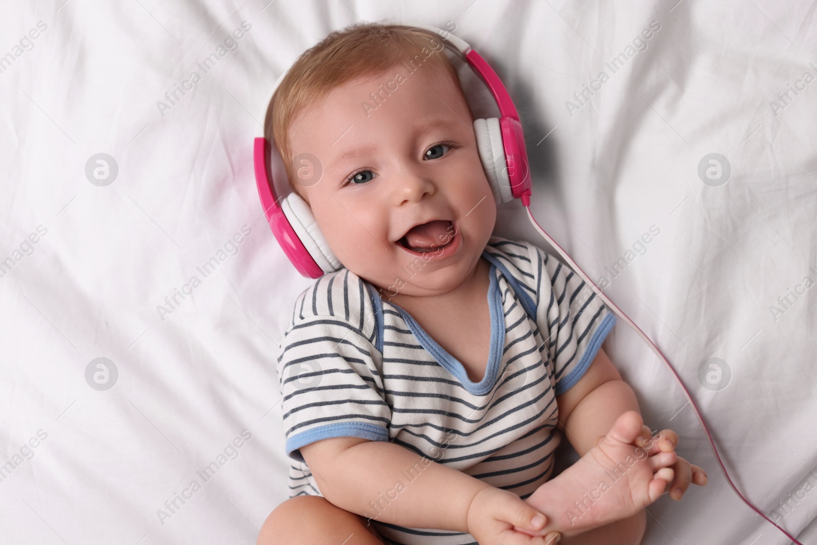 Photo of Cute little baby with headphones lying on bed, top view