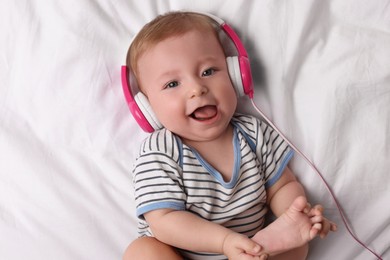 Cute little baby with headphones lying on bed, top view