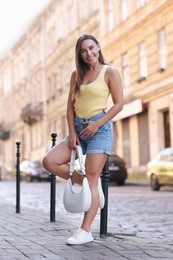 Photo of Beautiful woman with white bag wearing stylish denim shorts outdoors