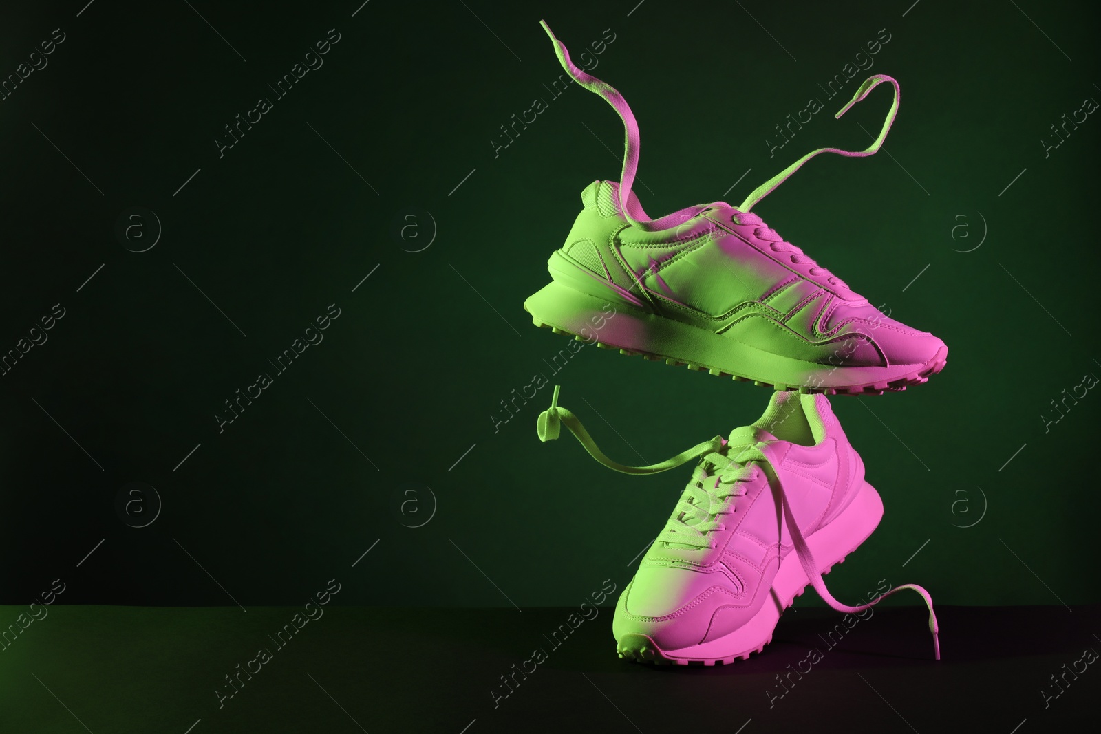 Photo of Pair of stylish sneakers in air against dark background in neon lights, space for text