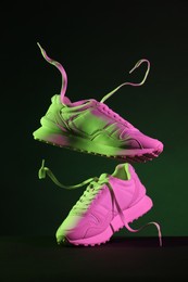 Photo of Pair of stylish sneakers in air against dark background in neon lights