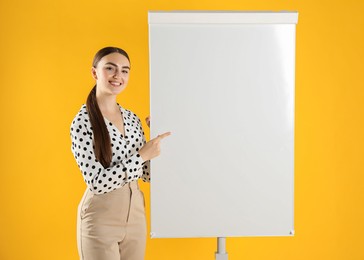 Photo of Happy woman near flip chart on orange background. Mockup for design