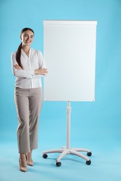 Photo of Happy woman near flip chart on light blue background. Mockup for design