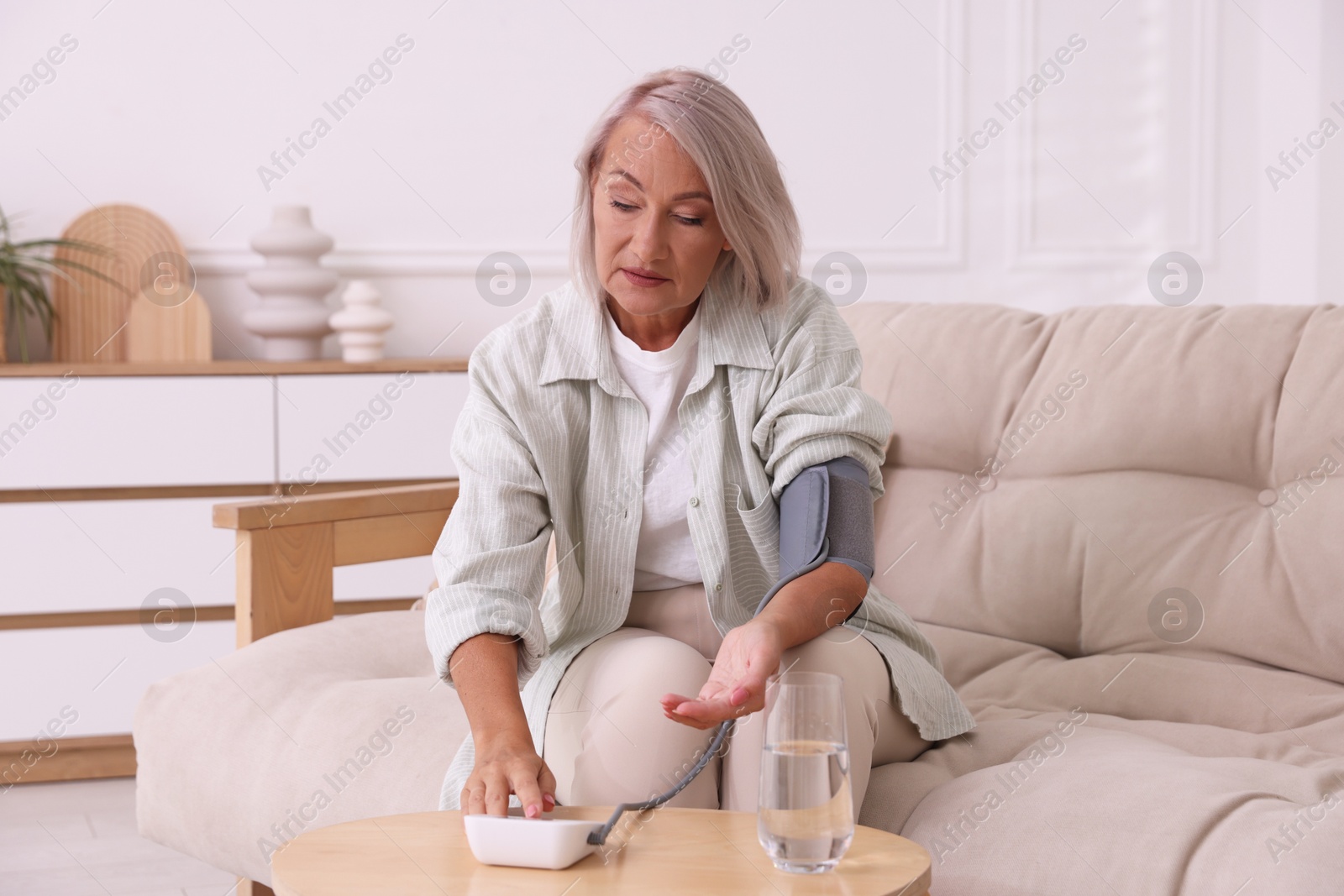 Photo of Woman measuring blood pressure on sofa indoors