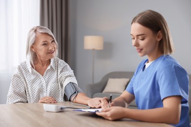 Photo of Healthcare worker measuring patient's blood pressure at wooden table indoors