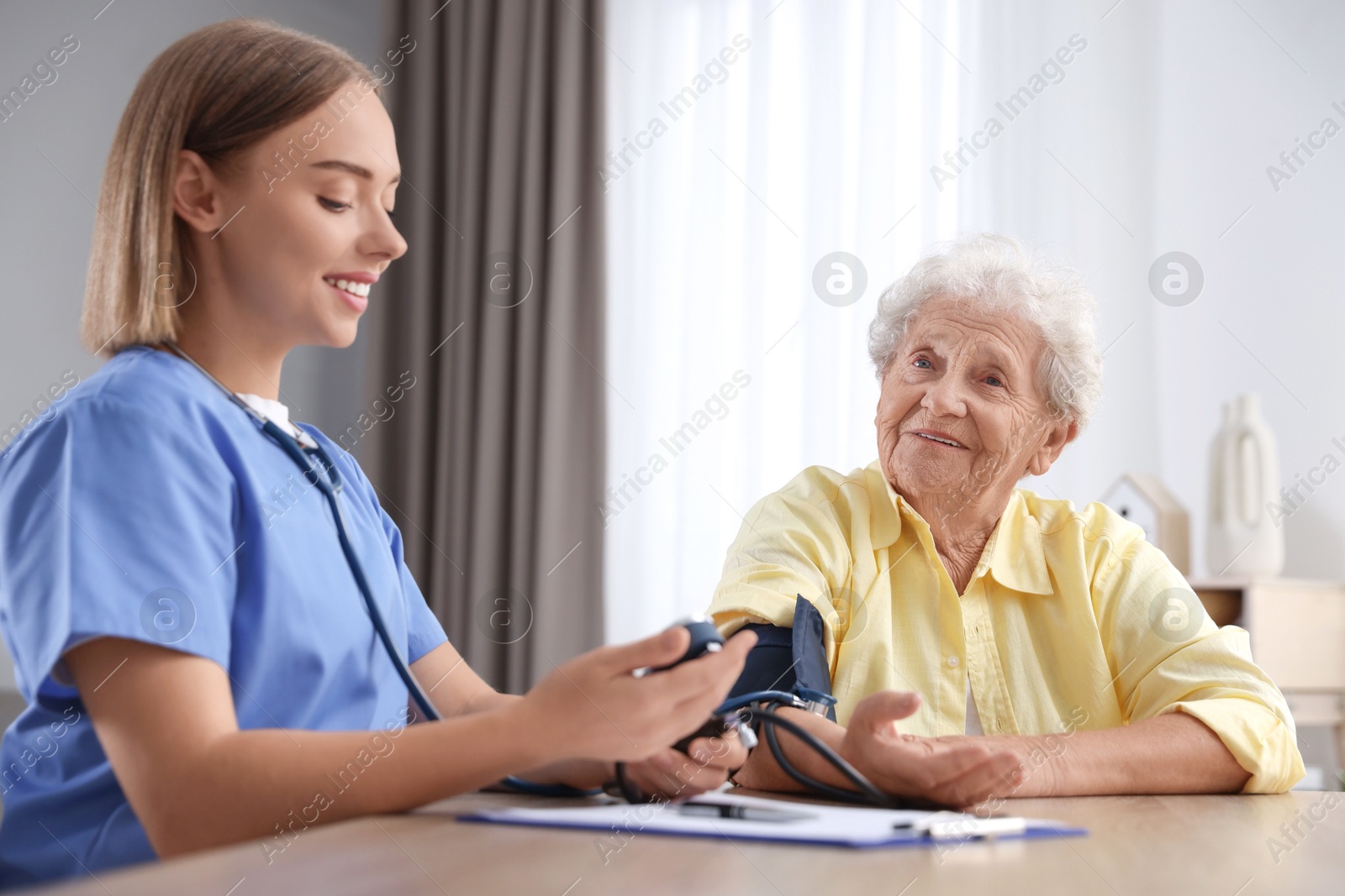 Photo of Healthcare worker measuring patient's blood pressure at wooden table indoors