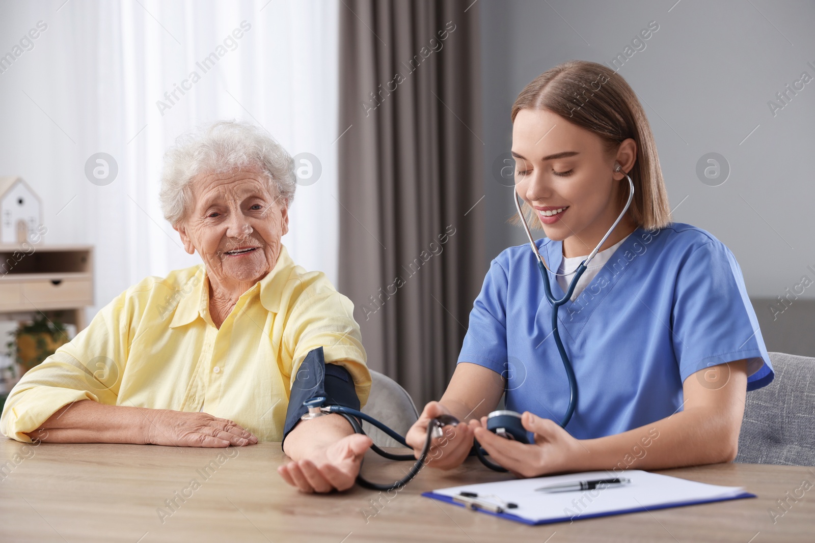 Photo of Healthcare worker measuring patient's blood pressure at wooden table indoors