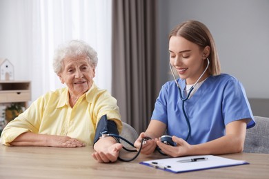 Photo of Healthcare worker measuring patient's blood pressure at wooden table indoors