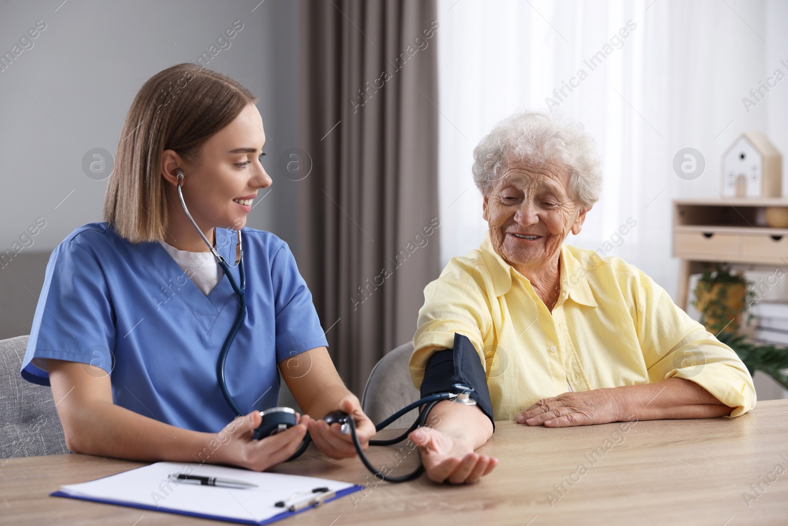 Photo of Healthcare worker measuring patient's blood pressure at wooden table indoors