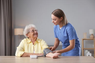 Healthcare worker measuring patient's blood pressure at wooden table indoors