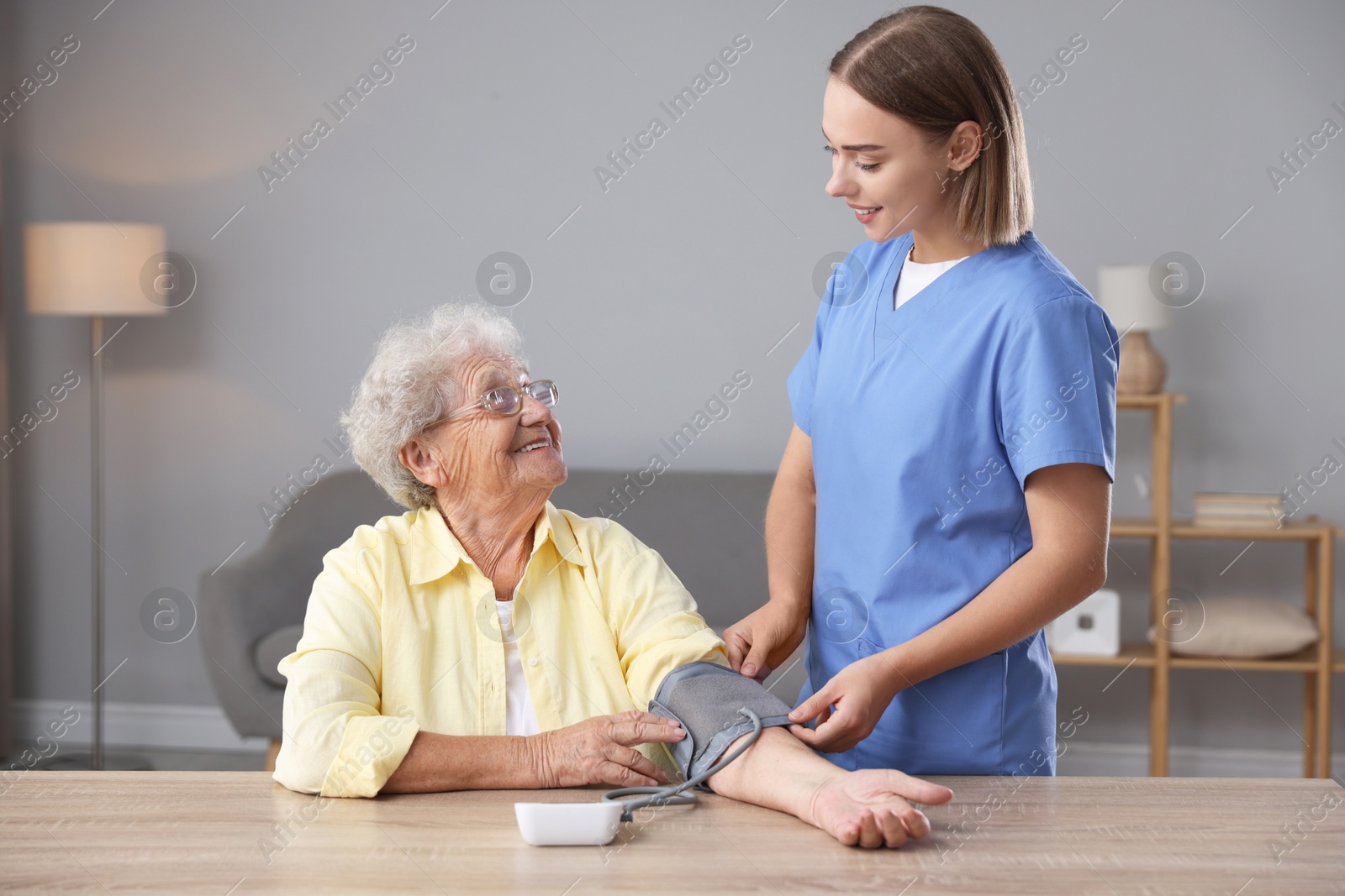 Photo of Healthcare worker measuring patient's blood pressure at wooden table indoors