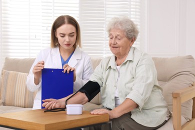 Photo of Doctor measuring patient's blood pressure at wooden table indoors