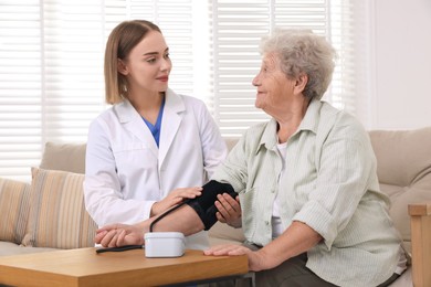 Doctor measuring patient's blood pressure at wooden table indoors