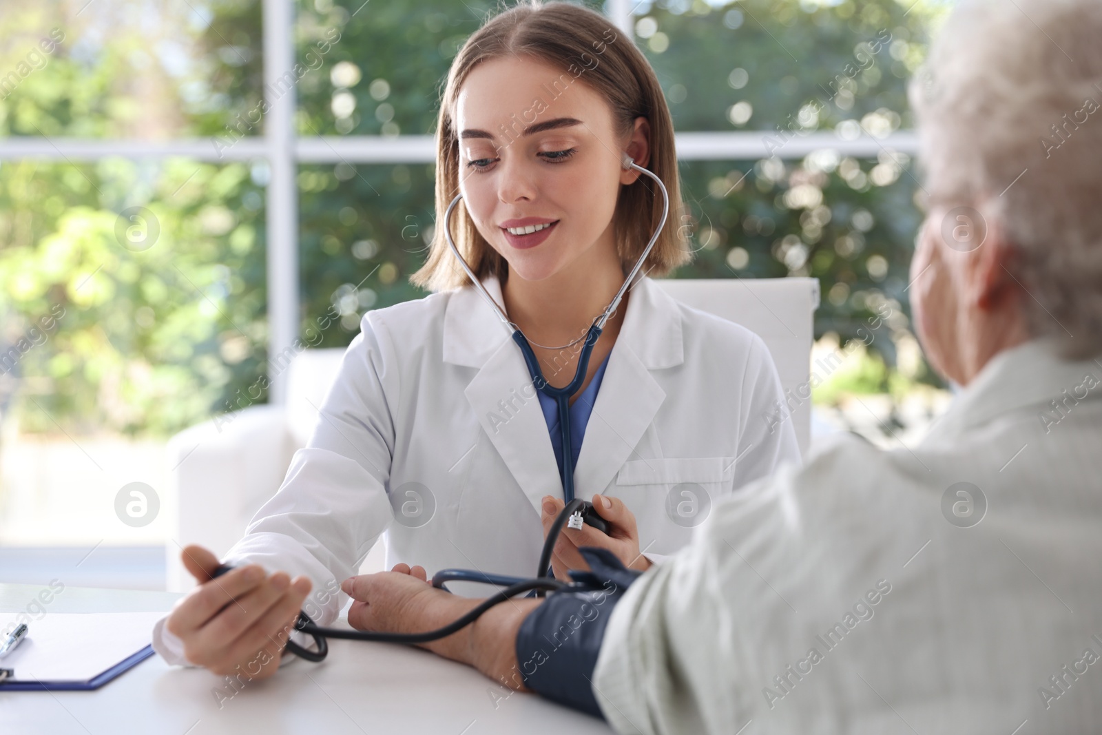 Photo of Doctor measuring patient's blood pressure at table in hospital