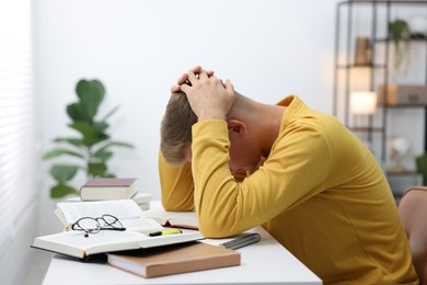 Photo of Tired student preparing for exam at table indoors