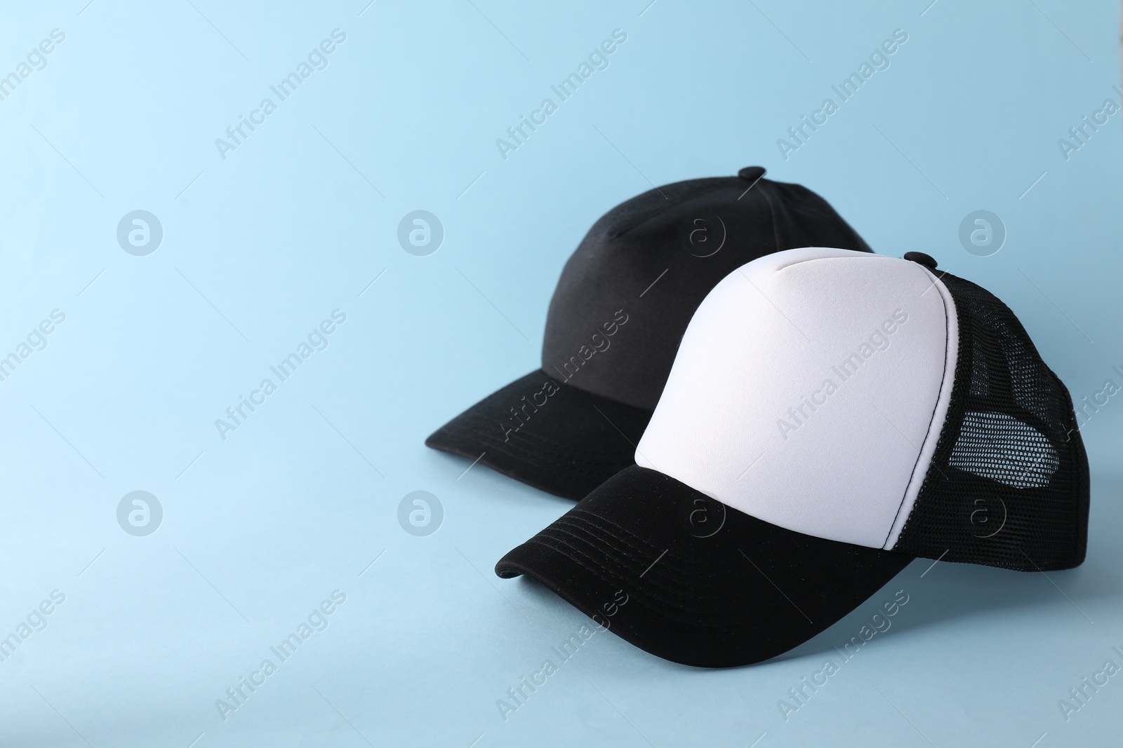 Photo of Stylish baseball caps on light blue background. Mockup for design