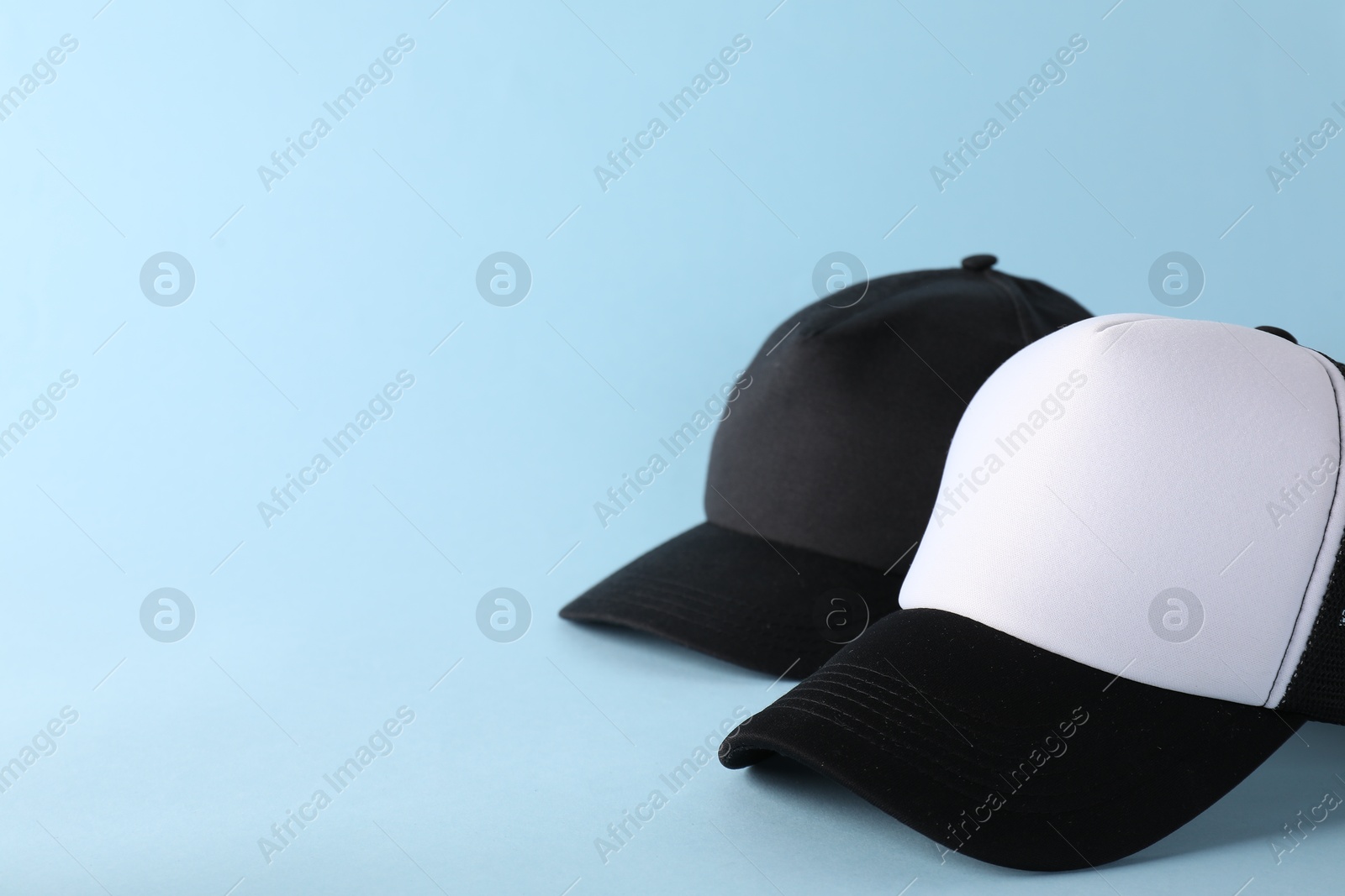 Photo of Stylish baseball caps on light blue background. Mockup for design