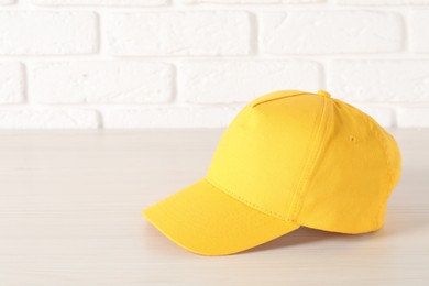 Photo of Stylish yellow baseball cap on wooden table. Mockup for design