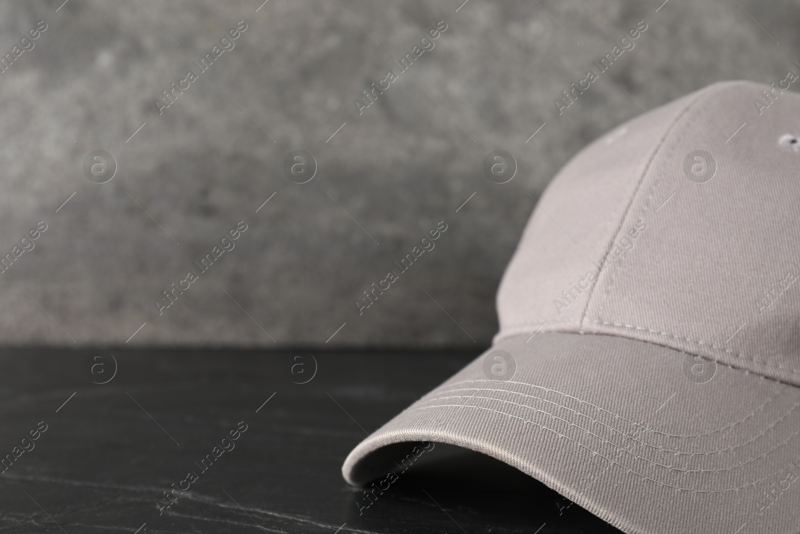 Photo of Stylish baseball cap on dark textured table, closeup. Mockup for design