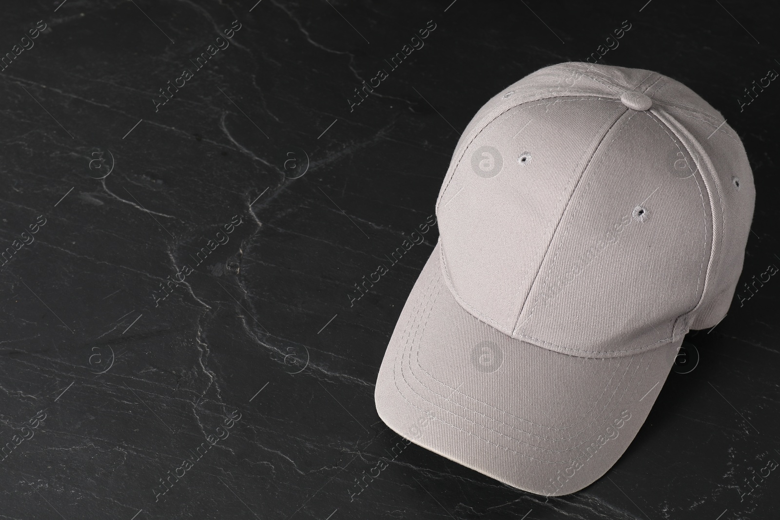 Photo of Stylish baseball cap on dark textured table. Mockup for design