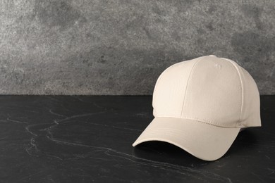 Photo of Stylish baseball cap on dark textured table. Mockup for design