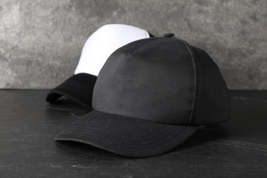 Photo of Stylish baseball caps on dark textured table, closeup. Mockup for design