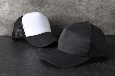 Photo of Stylish baseball caps on dark textured table. Mockup for design