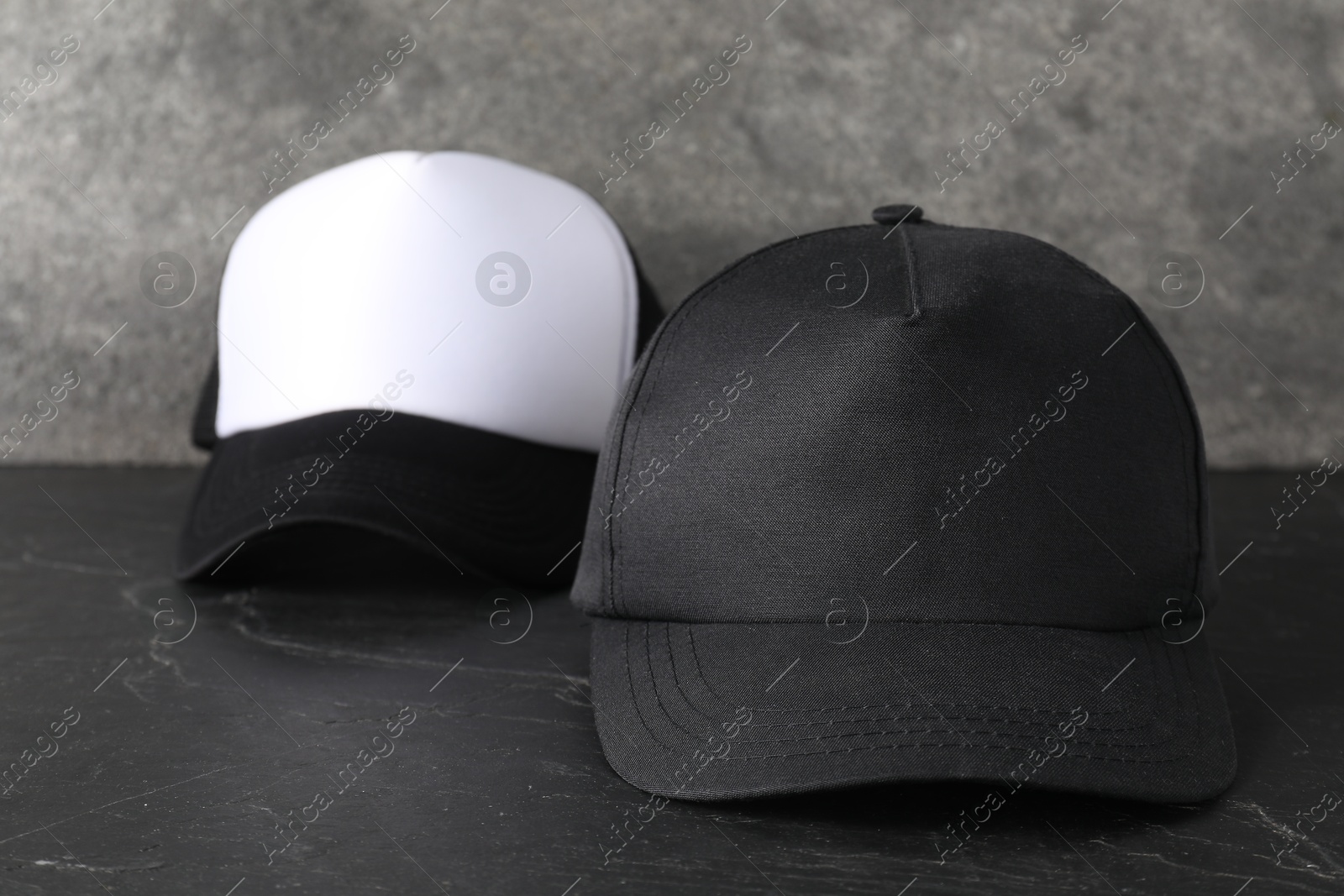 Photo of Stylish baseball caps on dark textured table, closeup. Mockup for design