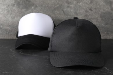 Photo of Stylish baseball caps on dark textured table, closeup. Mockup for design