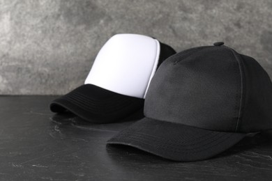 Photo of Stylish baseball caps on dark textured table, closeup. Mockup for design