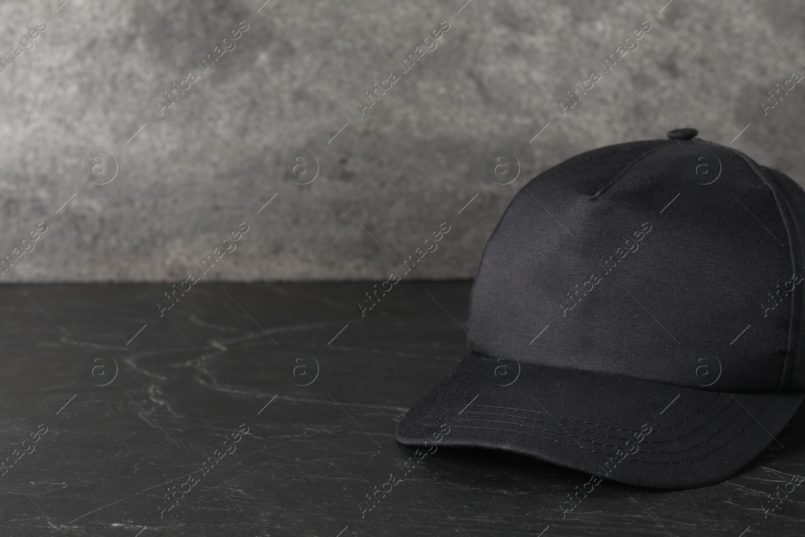 Photo of Stylish baseball cap on dark textured table, closeup. Mockup for design