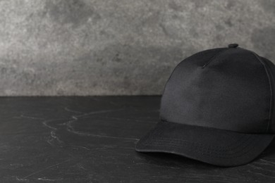 Photo of Stylish baseball cap on dark textured table, closeup. Mockup for design