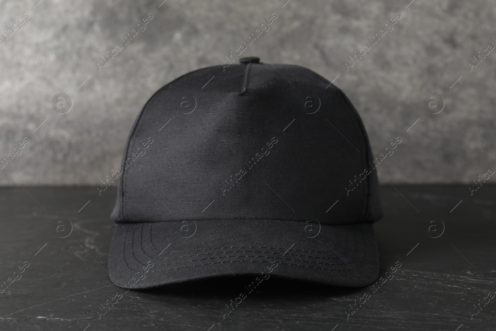 Photo of Stylish baseball cap on dark textured table, closeup. Mockup for design