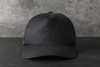 Photo of Stylish baseball cap on dark textured table, closeup. Mockup for design