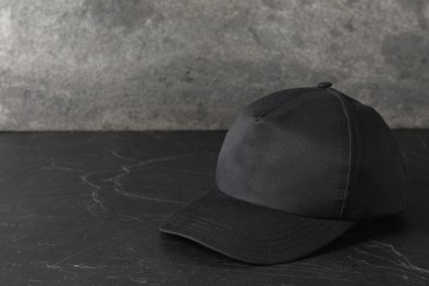 Photo of Stylish baseball cap on dark textured table. Mockup for design