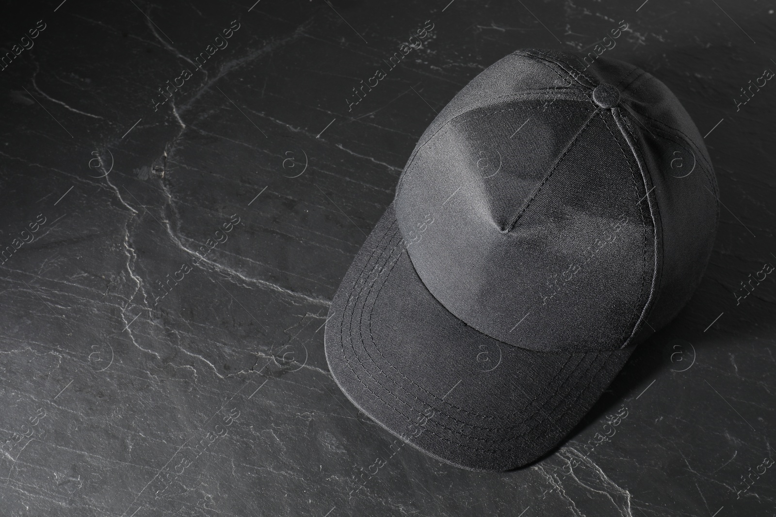 Photo of Stylish baseball cap on dark textured table, above view. Mockup for design