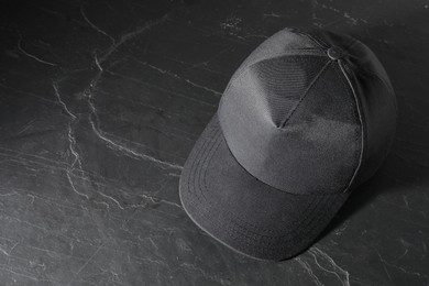 Photo of Stylish baseball cap on dark textured table, above view. Mockup for design