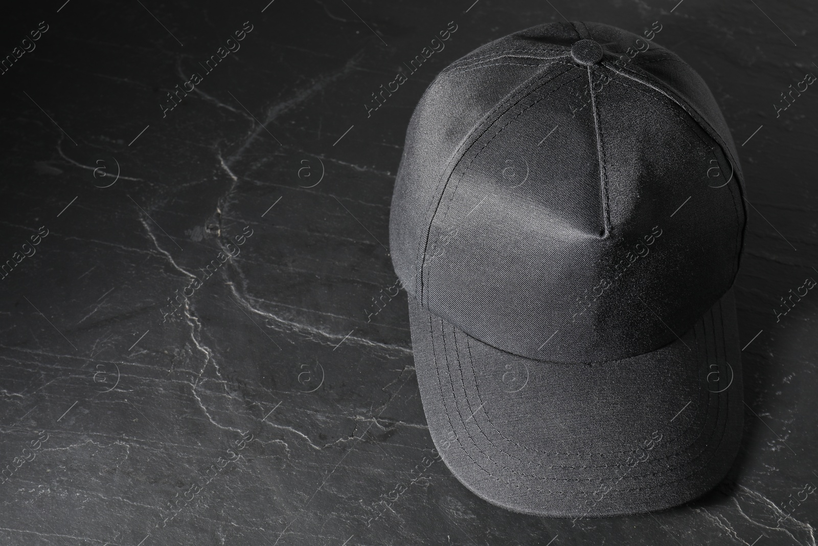 Photo of Stylish baseball cap on dark textured table. Mockup for design