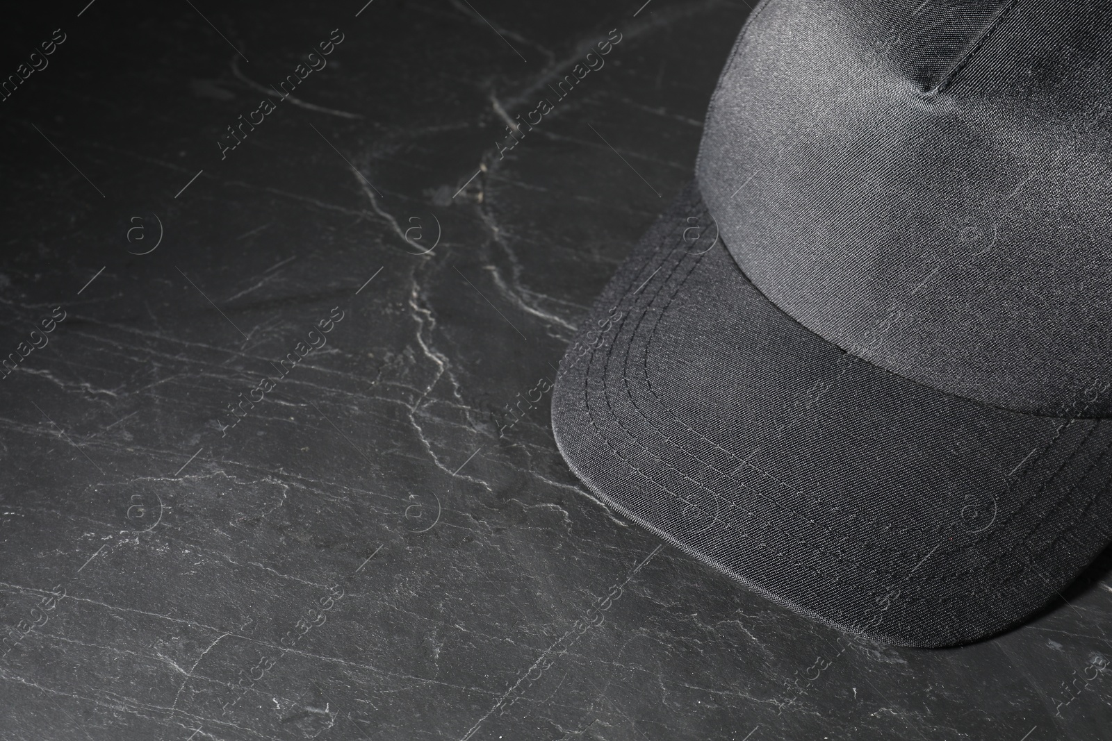 Photo of Stylish baseball cap on dark textured table, closeup. Mockup for design