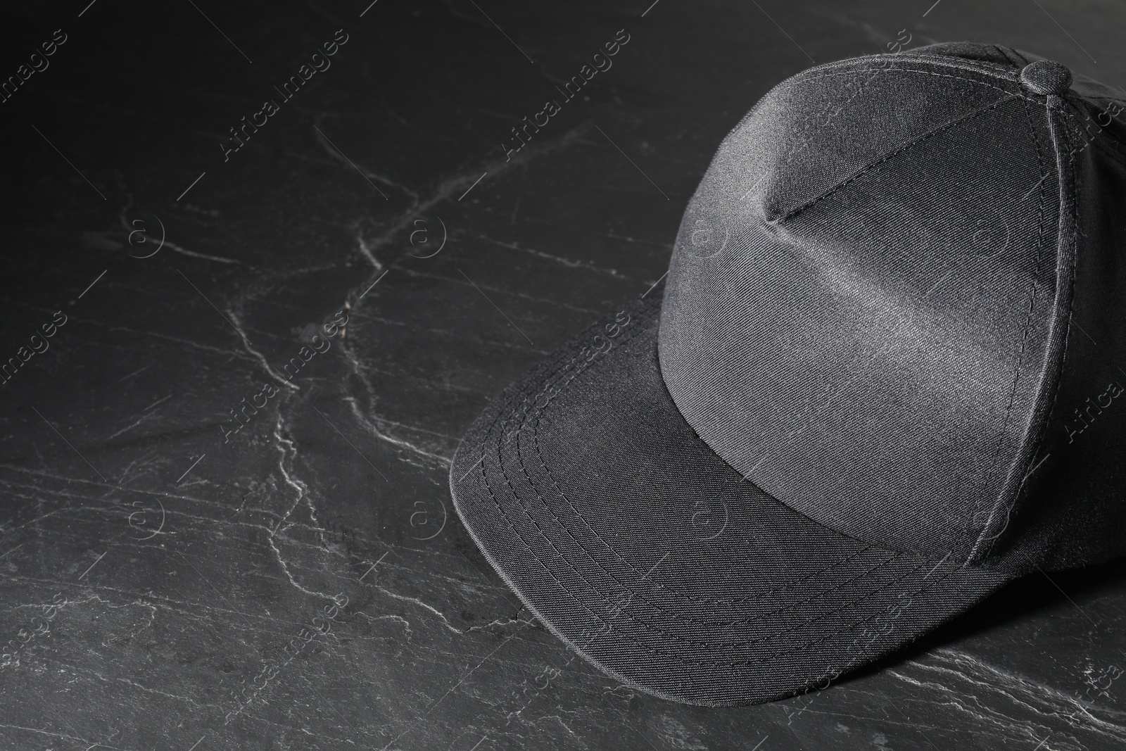 Photo of Stylish baseball cap on dark textured table. Mockup for design