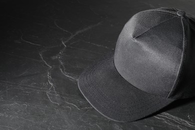 Photo of Stylish baseball cap on dark textured table. Mockup for design