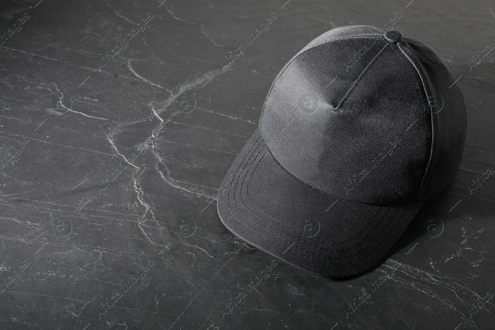 Photo of Stylish baseball cap on dark textured table. Mockup for design