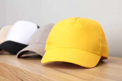 Photo of Stylish baseball caps on wooden table, closeup. Mockup for design