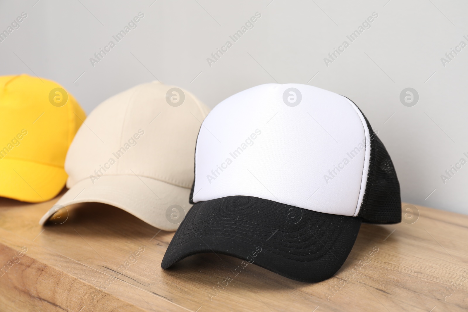 Photo of Stylish baseball caps on wooden table, closeup. Mockup for design