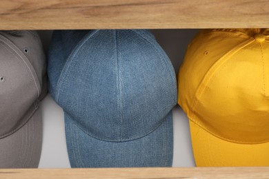 Photo of Stylish baseball caps in chest of drawers, closeup. Mockup for design