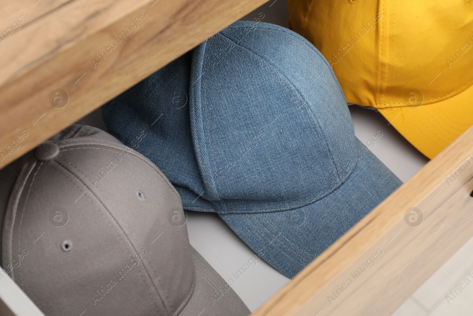 Photo of Stylish baseball caps in chest of drawers, closeup. Mockup for design