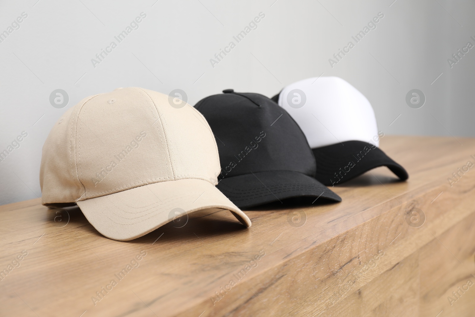 Photo of Stylish baseball caps on wooden chest of drawers. Mockup for design